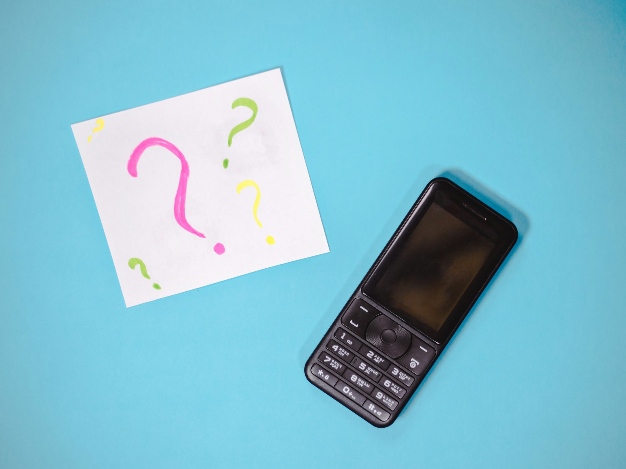 Old mobile telephone isolated on blue background. Paper with question marks